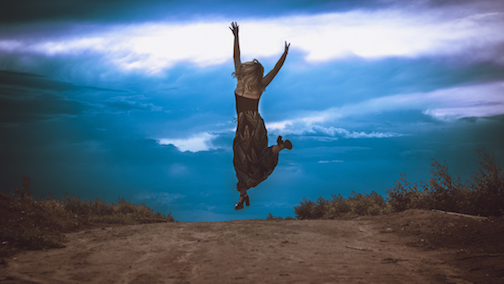 Woman jumping up with joy with clouds in the background. 
